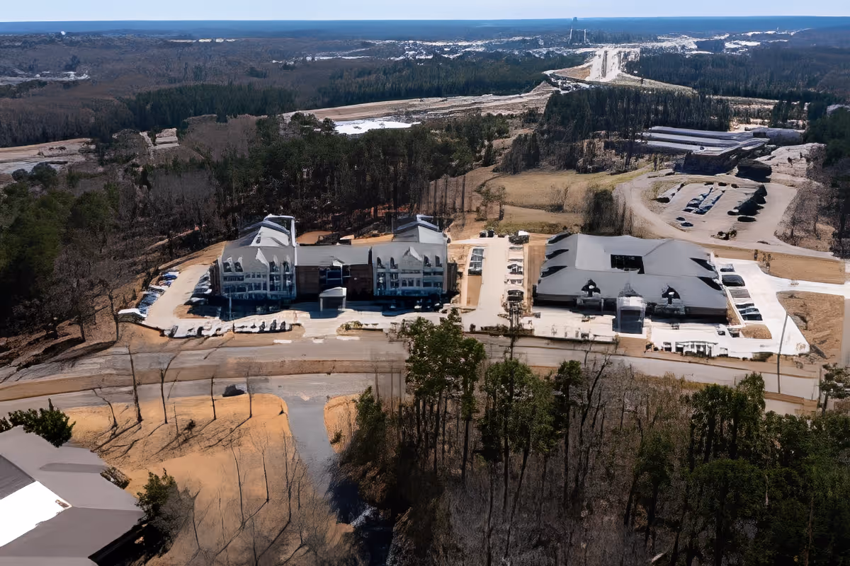 Aerial view of SummerHouse Beau Ridge facility showing multiple buildings surrounded by trees and parking areas, with a road in front and forested landscape in the background.