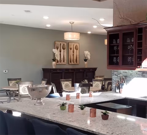 Open kitchen with a large marble island in the foreground and a dining area with chairs, buffet cabinet, and wall art in the background.