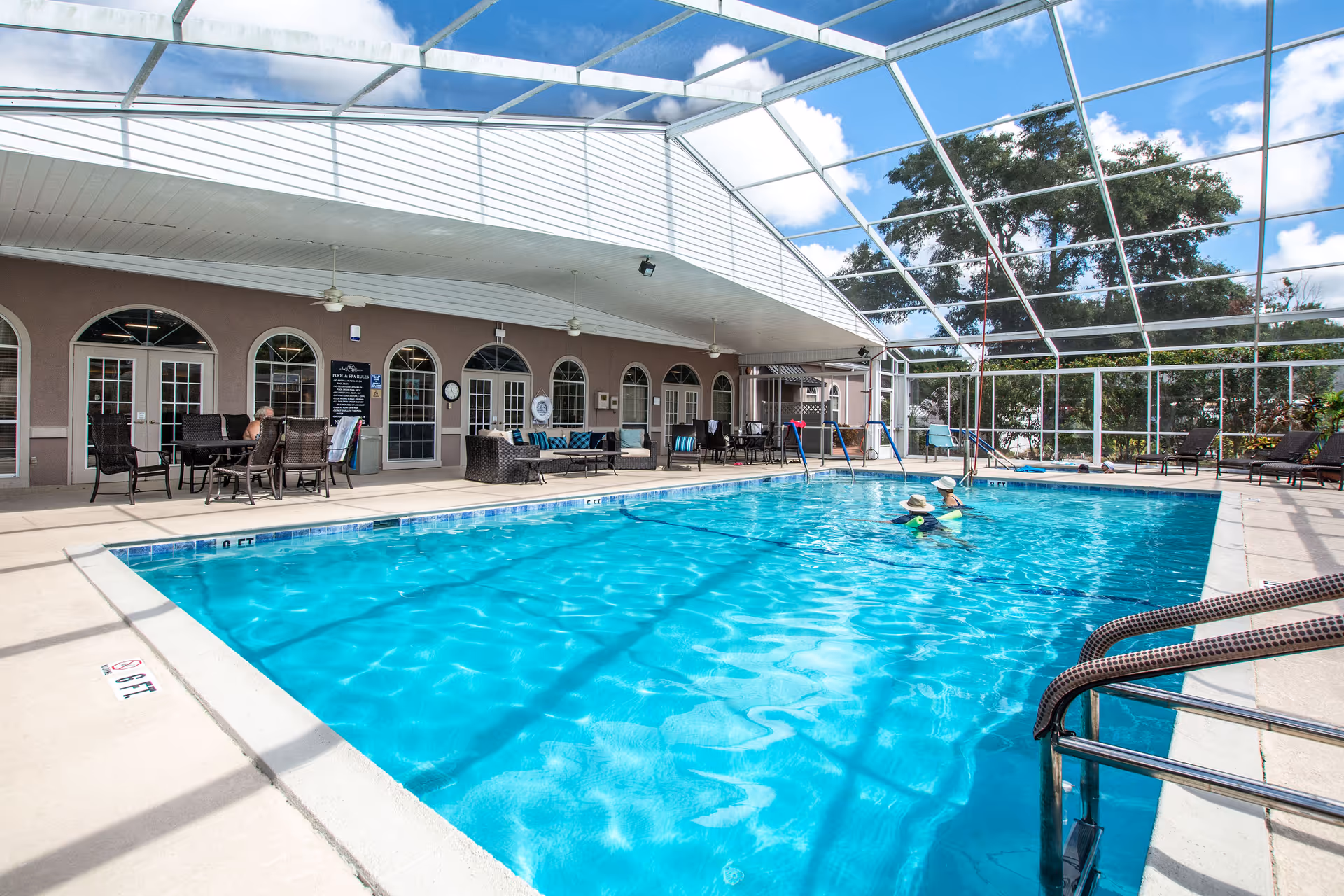 A screened indoor pool with lounge chairs, tables and a covered seating area while two people swim.