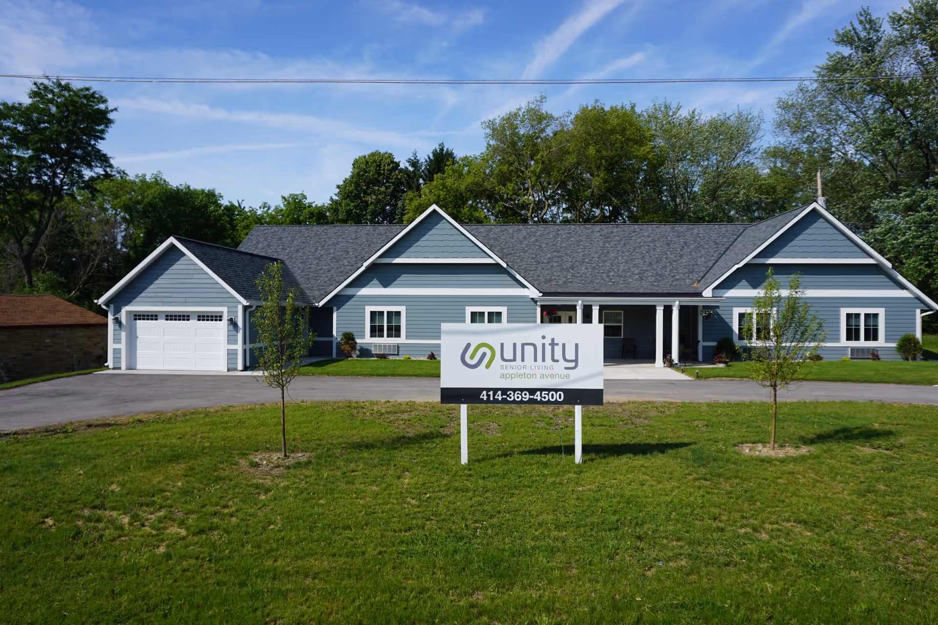Front exterior of a single-story blue senior living building with a lawn and a 'Unity Senior Living' sign in the foreground.