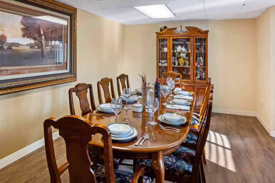 A formal dining room with a polished wooden table set for a meal, matching chairs, and a china cabinet against the far wall.