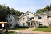 A beige senior living facility exterior with an entrance porch and outdoor seating area.