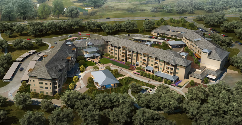 Aerial view of a multi-wing senior living complex with landscaped courtyards, pathways, parking areas, and surrounding trees.