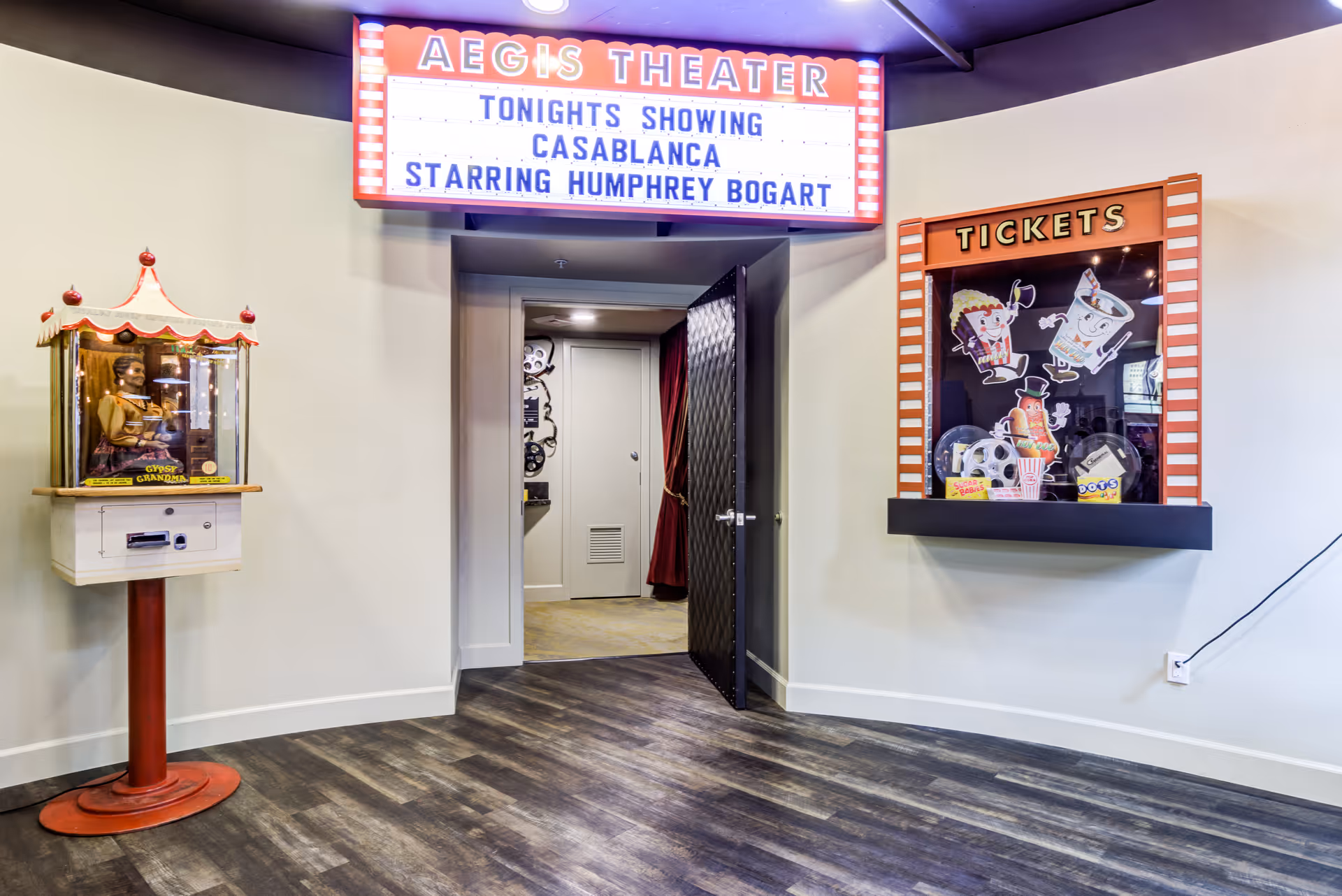 Interior view of Aegis Theater entrance with a marquee sign displaying 'Tonight's Showing Casablanca Starring Humphrey Bogart'. To the left is a vintage Gypsy Grandma fortune teller machine, and to the right is a ticket booth decorated with cartoon images of popcorn, soda, and candy.
