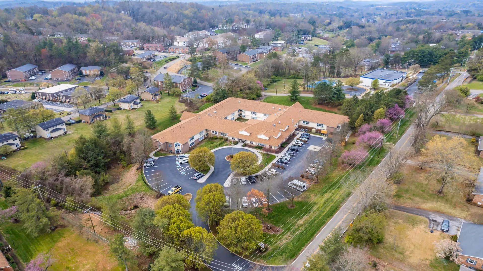 Aerial view of the American House West Knoxville senior living building with a circular driveway, parking lot, and surrounding neighborhood.