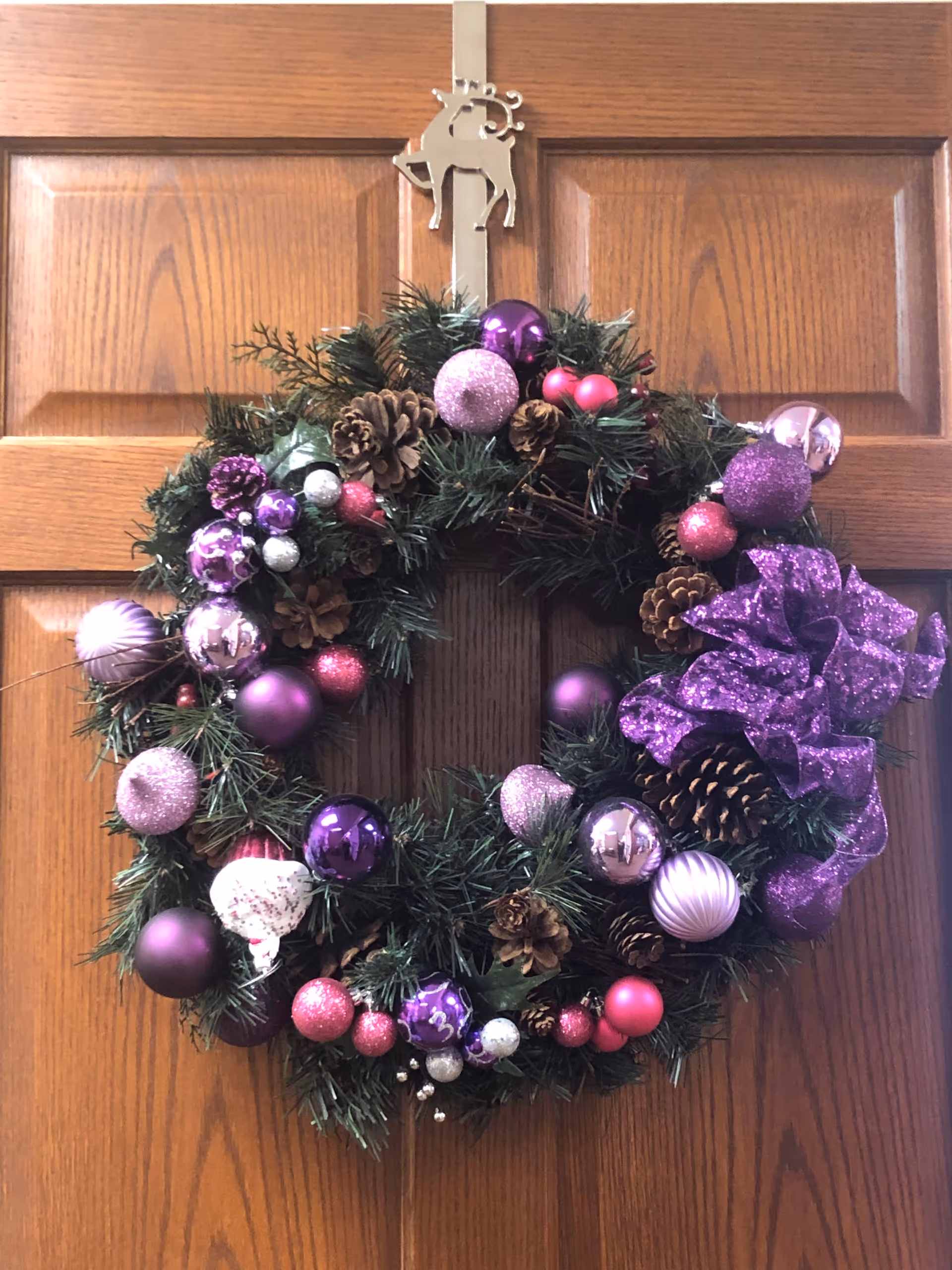 Decorative holiday wreath with purple ornaments and a bow hanging on a wooden door.