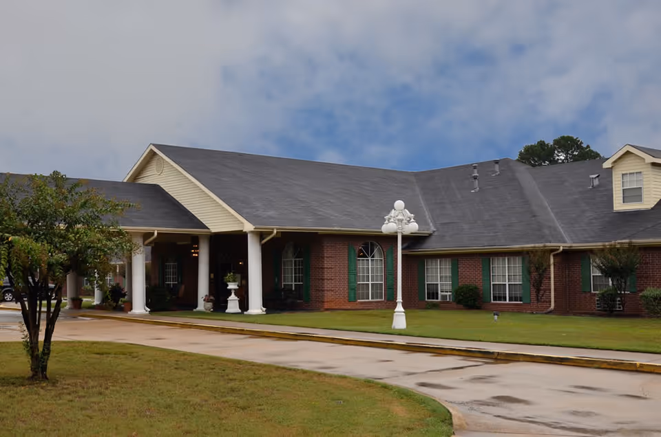 Front exterior of a single-story brick senior care building with a covered entrance supported by white columns and a driveway.