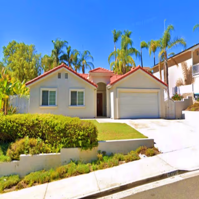 Single-story stucco house with a red tile roof, two-car garage, front lawn and palm trees.