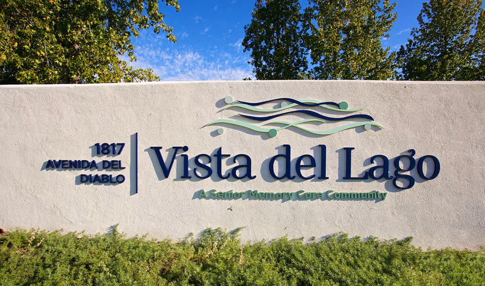 Entrance sign on a white stucco wall reading "Vista del Lago" with the address "1817 Avenida Del Diablo" and shrubs in front.