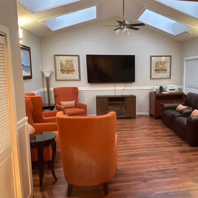 Cozy living room with orange upholstered chairs, a wall-mounted TV, skylights, and hardwood floors.