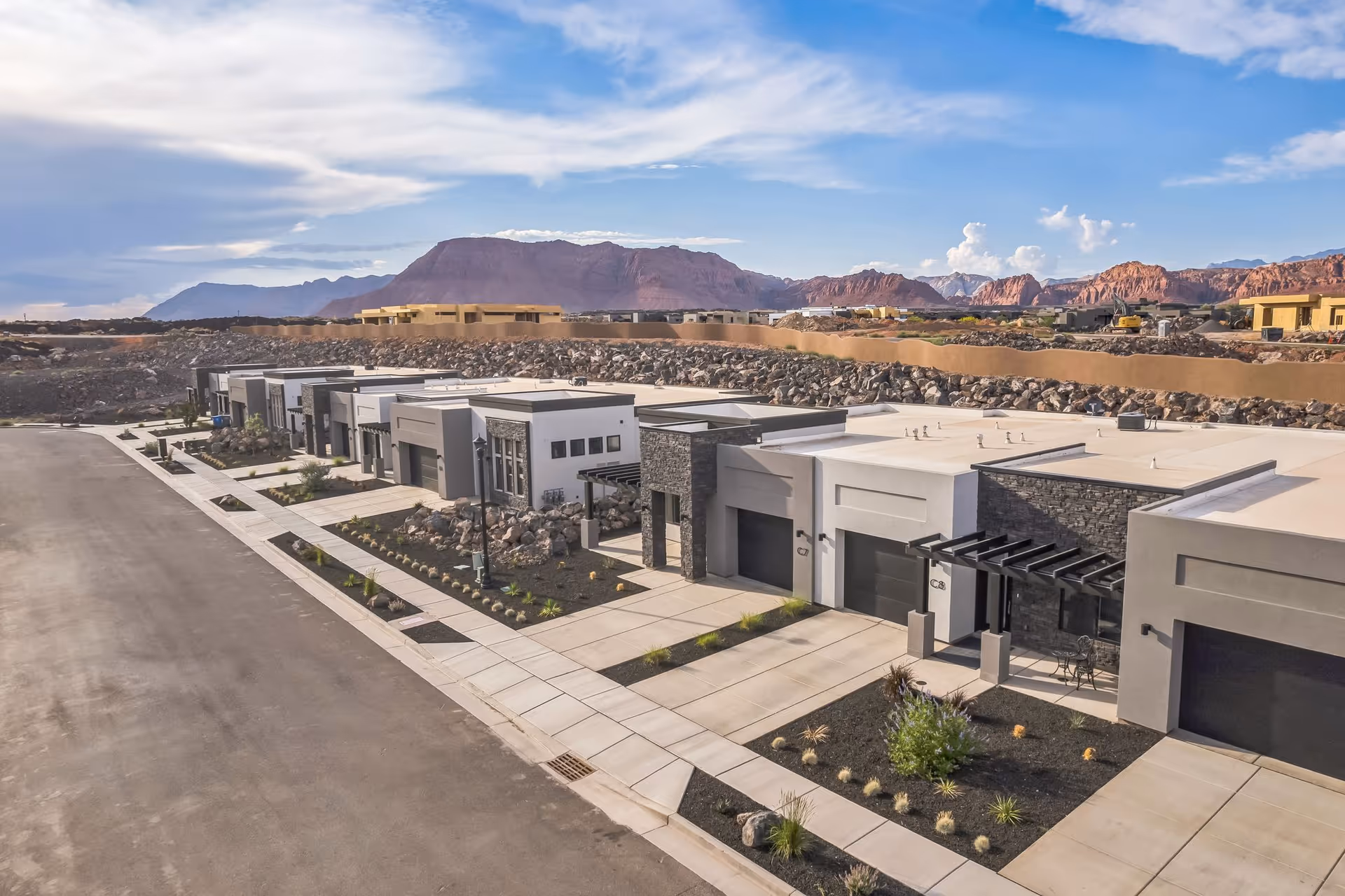 Aerial view of a row of modern single-story retirement community units with garages, landscaping, and red rock mountains in the background.