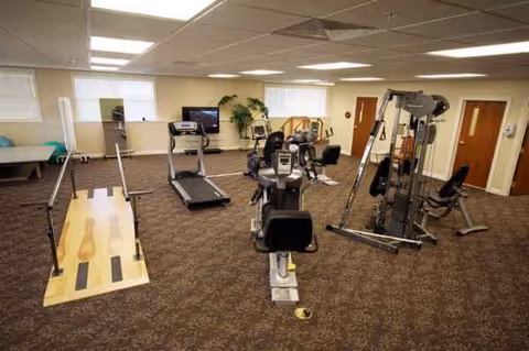 Indoor senior living gym with treadmills, weight machines, and cardio equipment in a carpeted, well-lit room.