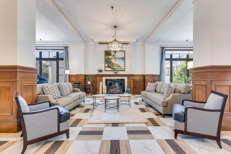 Elegant communal living room with sofas and armchairs arranged around a central coffee table and fireplace.