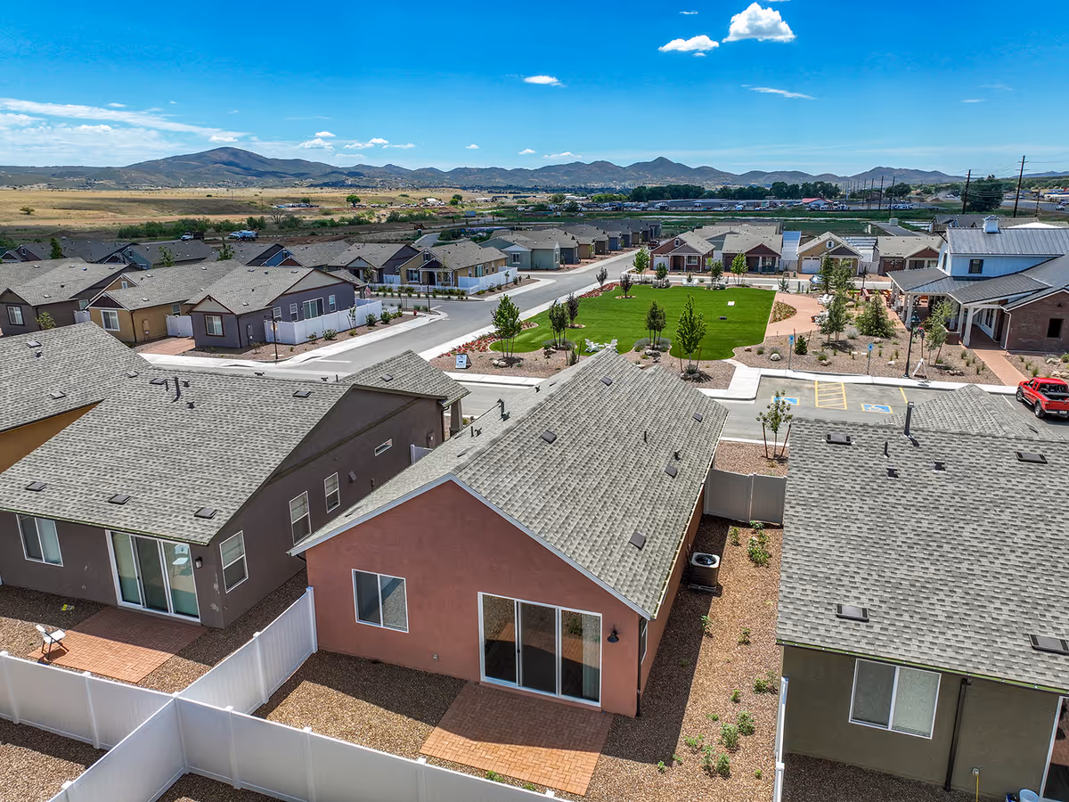 Aerial view of single-story cottages arranged around a central lawn and walkways in a senior living community with mountains in the distance.