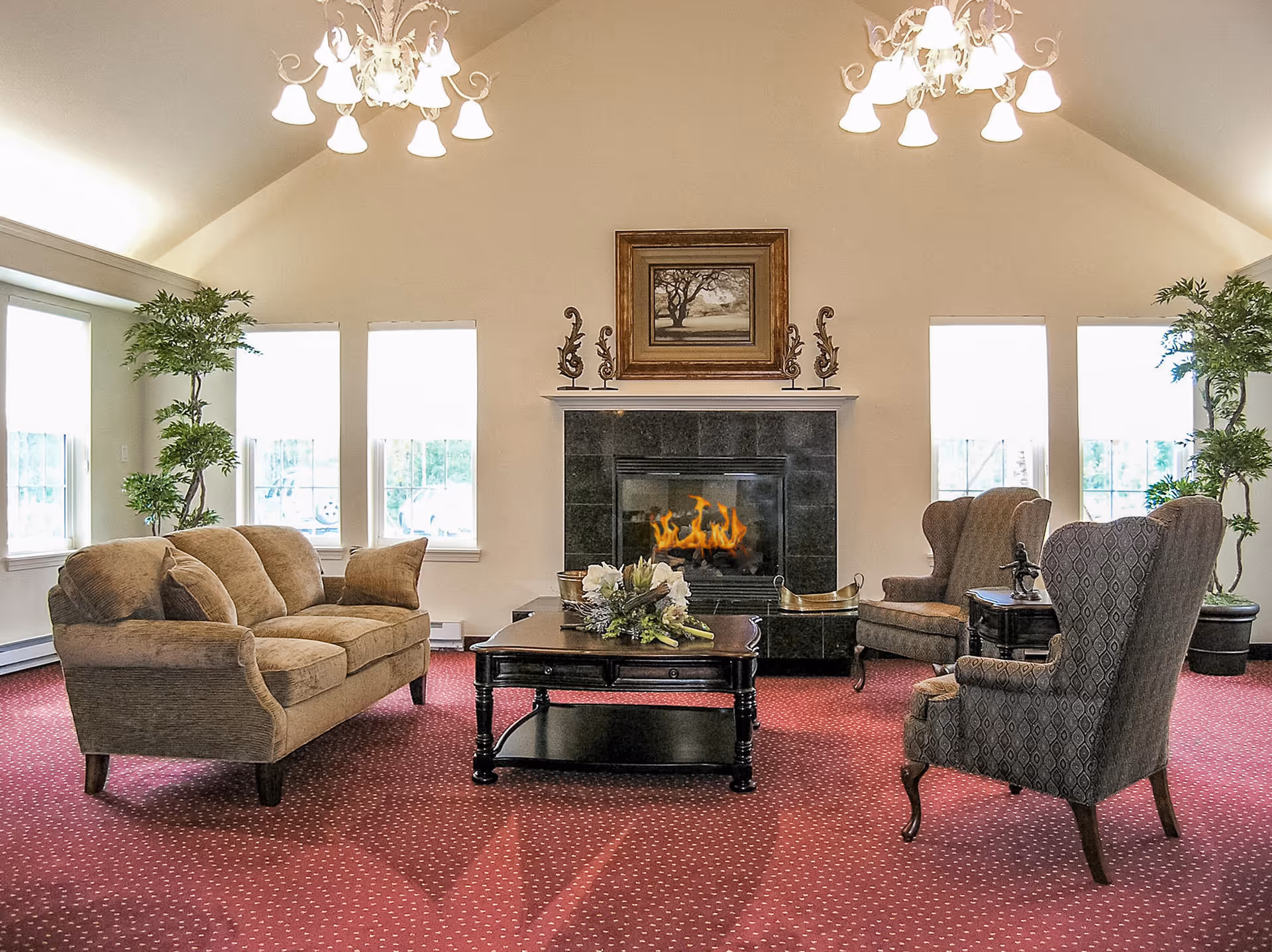 Spacious living room with sofa and armchairs arranged around a coffee table in front of a lit fireplace under a vaulted ceiling.