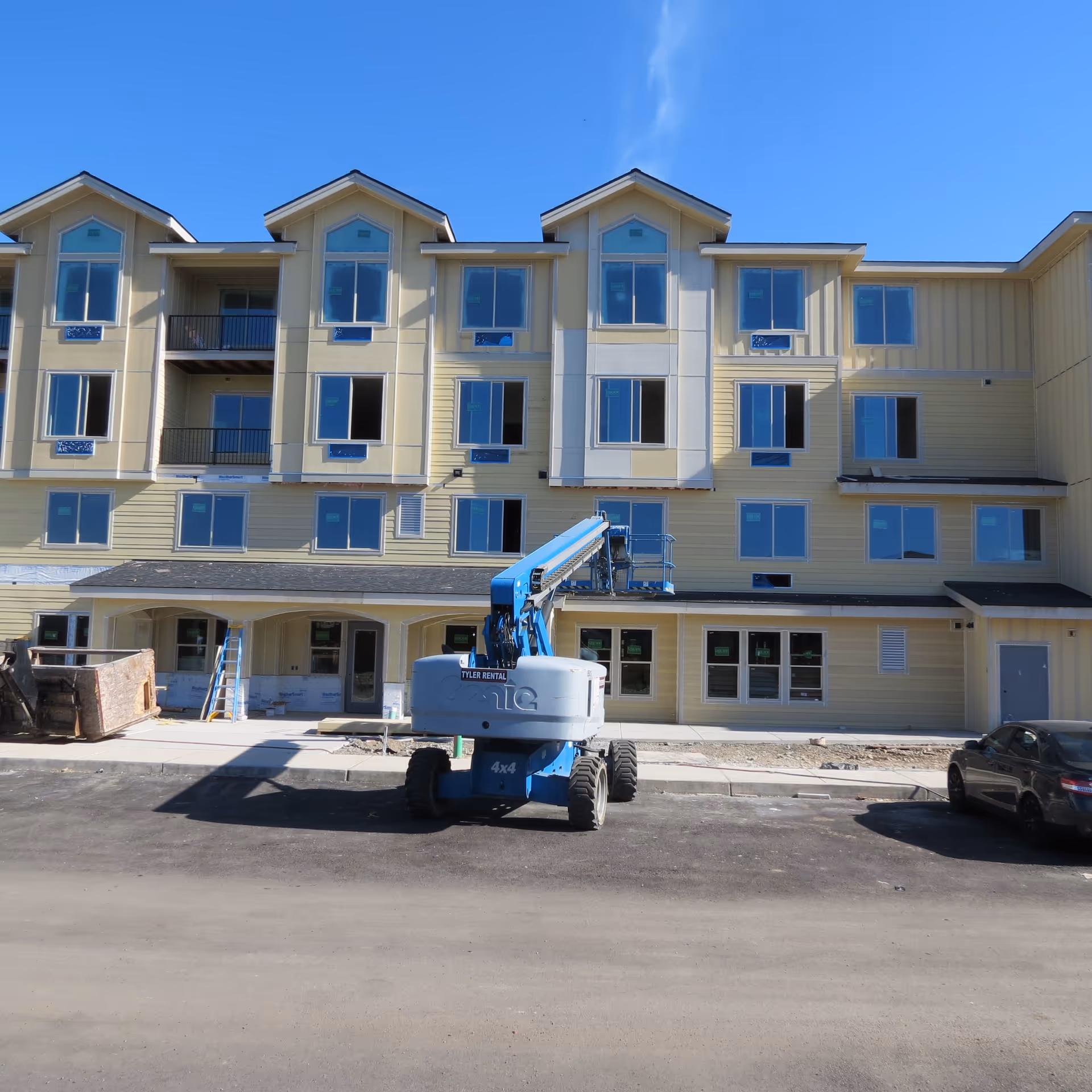 Front view of a multi-story senior living building under construction with a blue aerial lift parked in front.