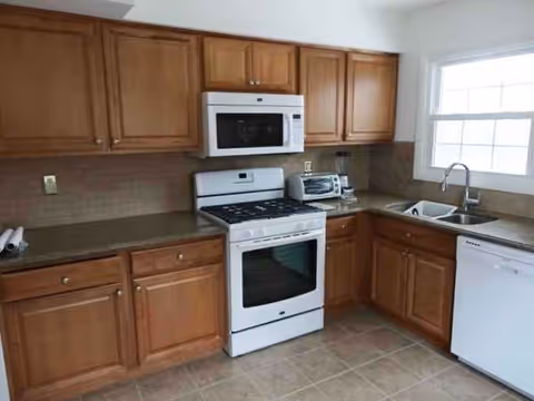 Kitchen with wooden cabinets, white stove, microwave, sink, and dishwasher.