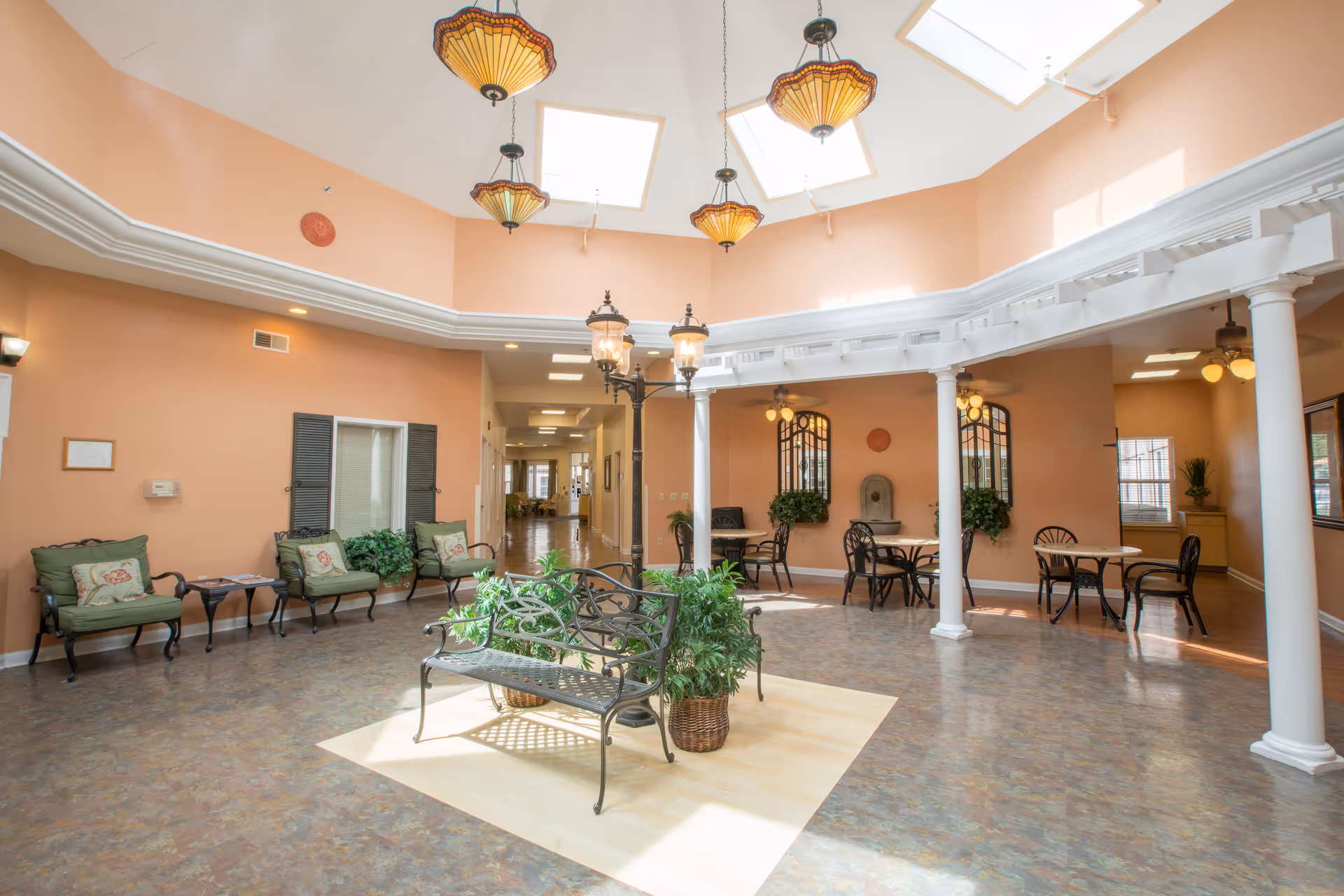 Sunlit atrium-style common area with benches, chairs, small tables, columns and skylights.