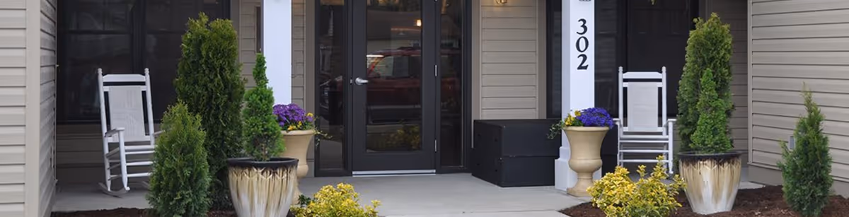 Front entrance with glass double doors, column marked 302, rocking chairs and potted plants on the porch.