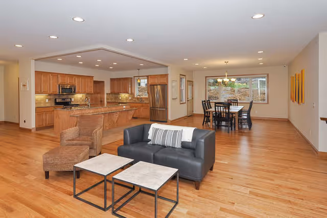 Open-plan living area with a sofa and small coffee tables facing an open kitchen and a dining table in the background.