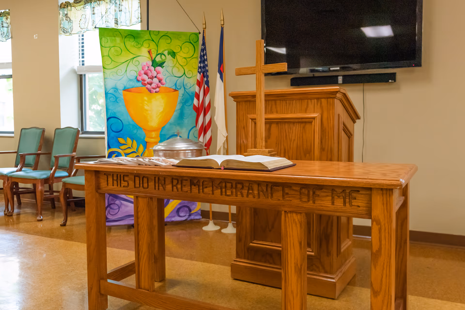 Wooden communion table and lectern in a chapel interior with an open Bible, cross, flags, and a colorful banner.