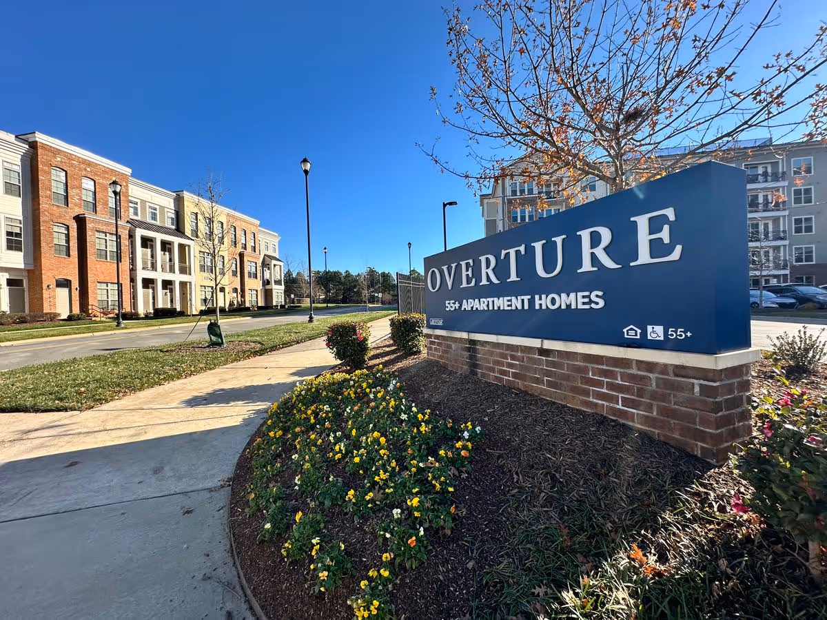 Entrance sign for Overture 55+ apartment homes with landscaped flowerbeds and apartment buildings in the background.