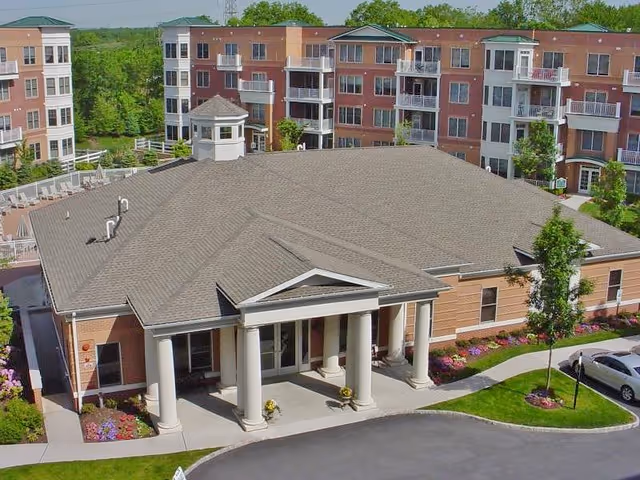 Front entrance of a senior living complex with a columned portico and surrounding multi-story apartment buildings.