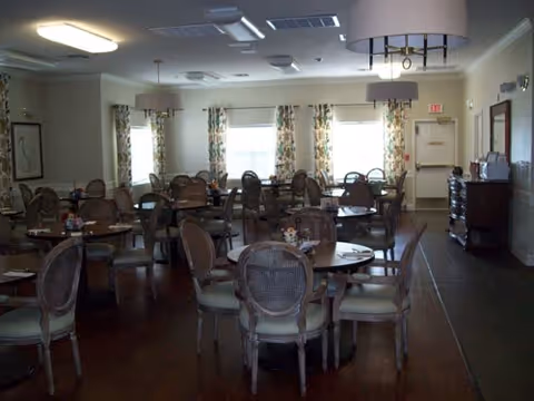 Dining room with multiple round tables and chairs, floral curtains, and overhead lighting.