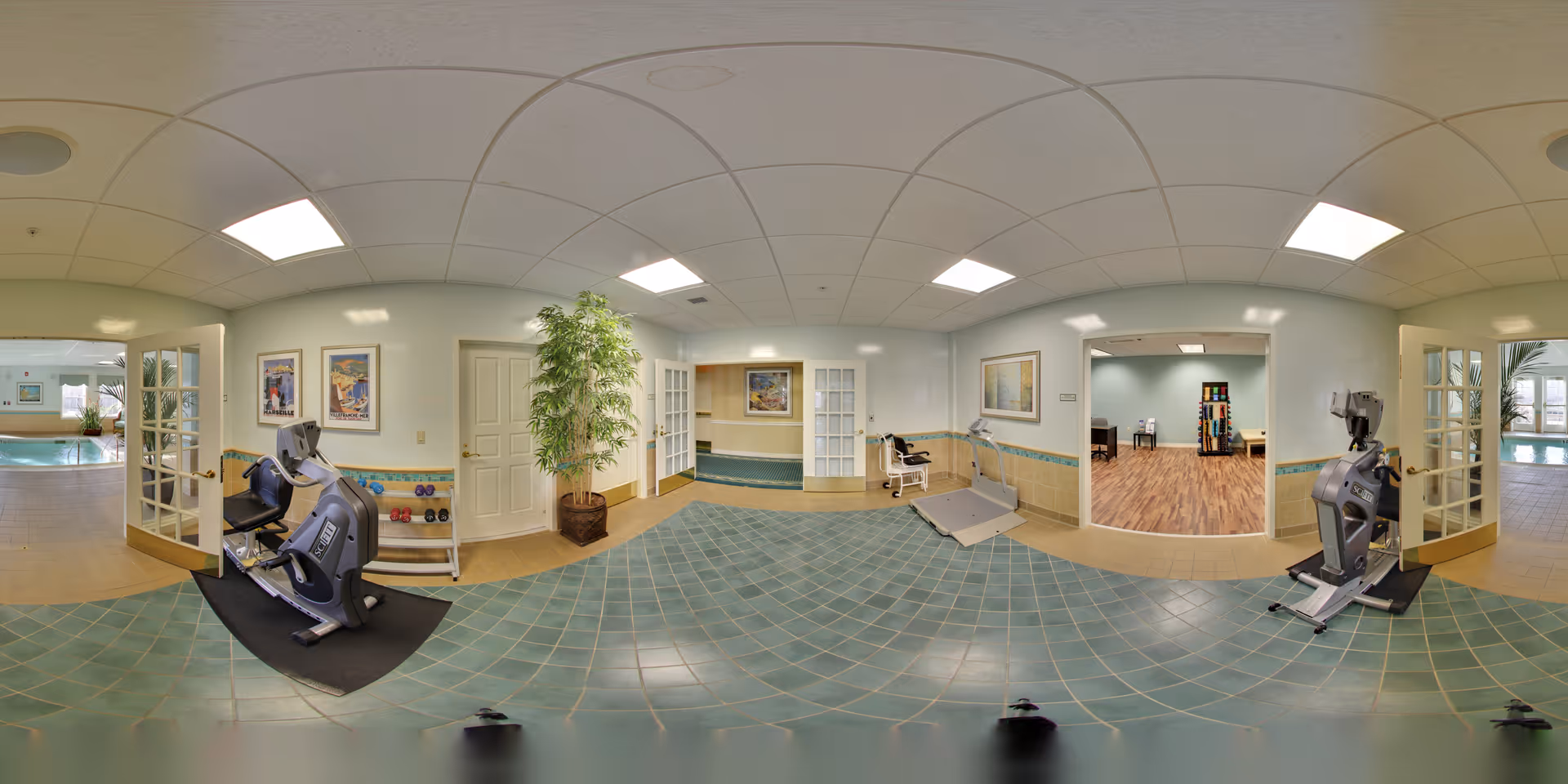 A spacious fitness and rehabilitation area with exercise equipment including stationary bikes and a treadmill. The room has tiled floors and light-colored walls with framed artwork. There are two open doorways leading to a room with wooden flooring and another area with a swimming pool visible through glass doors.