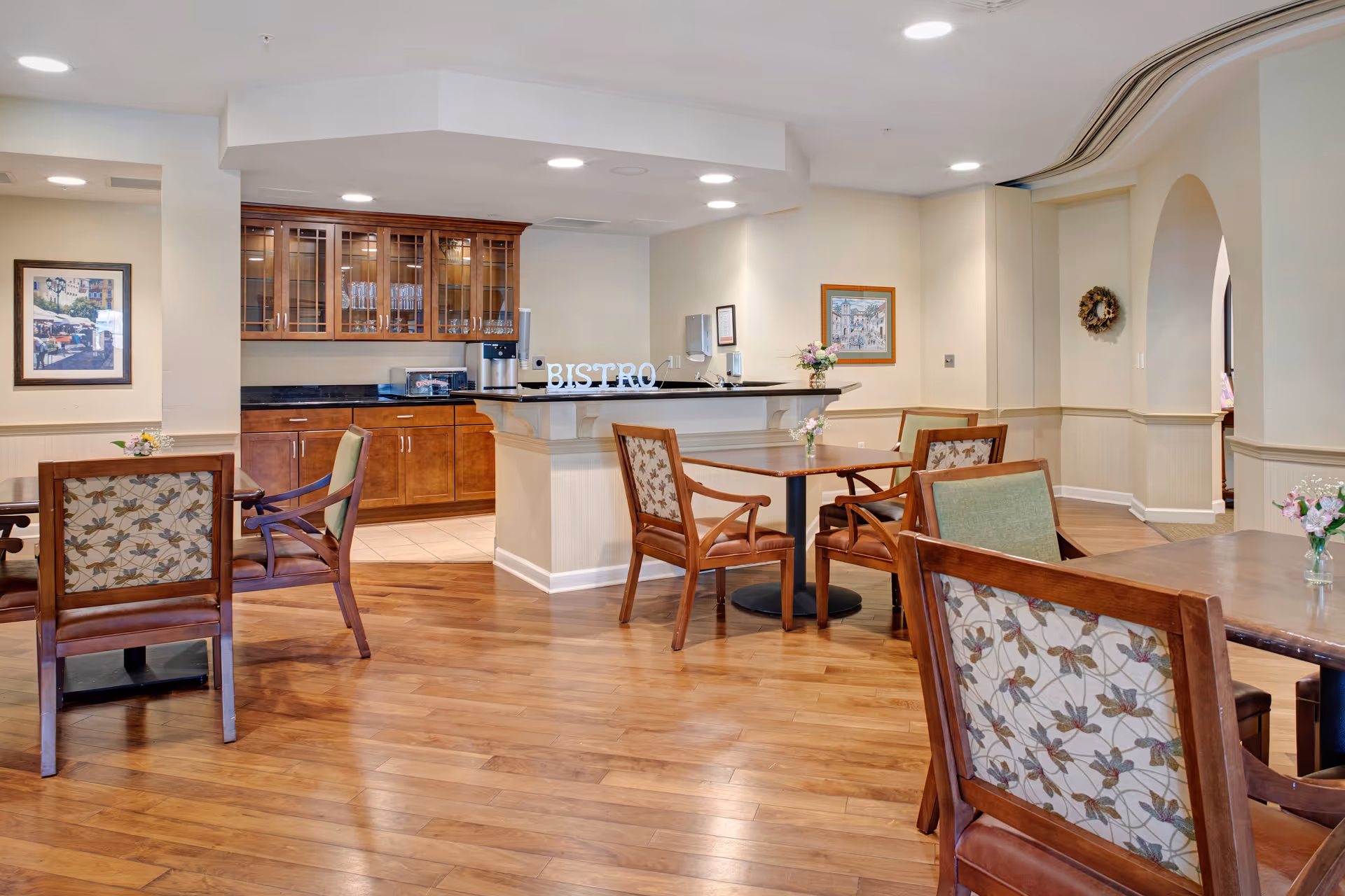 Interior bistro-style dining area with wooden floors, tables, upholstered chairs, and a serving counter.