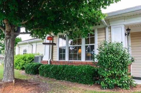 Exterior view of Summer Village Camellia Place front with shrubs, trees, and windows.