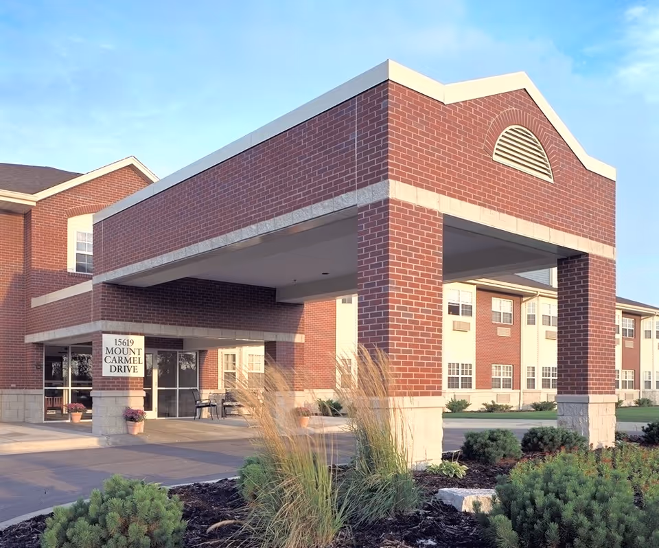 Exterior brick senior living building with covered entrance and landscaping.