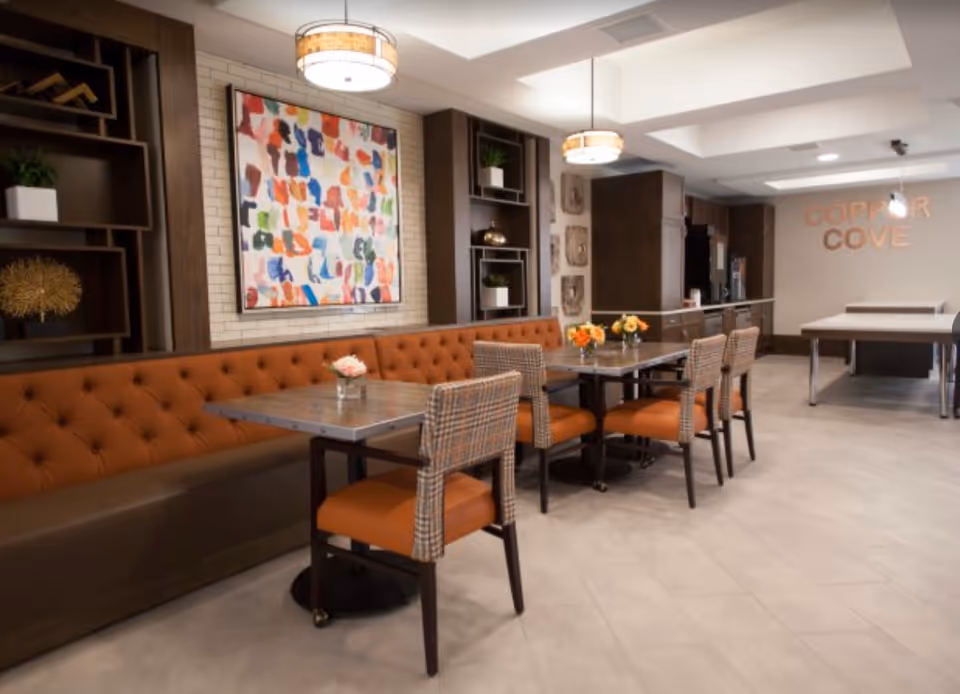 A modern dining area with tufted banquette seating, tables and chairs and colorful artwork on the wall.