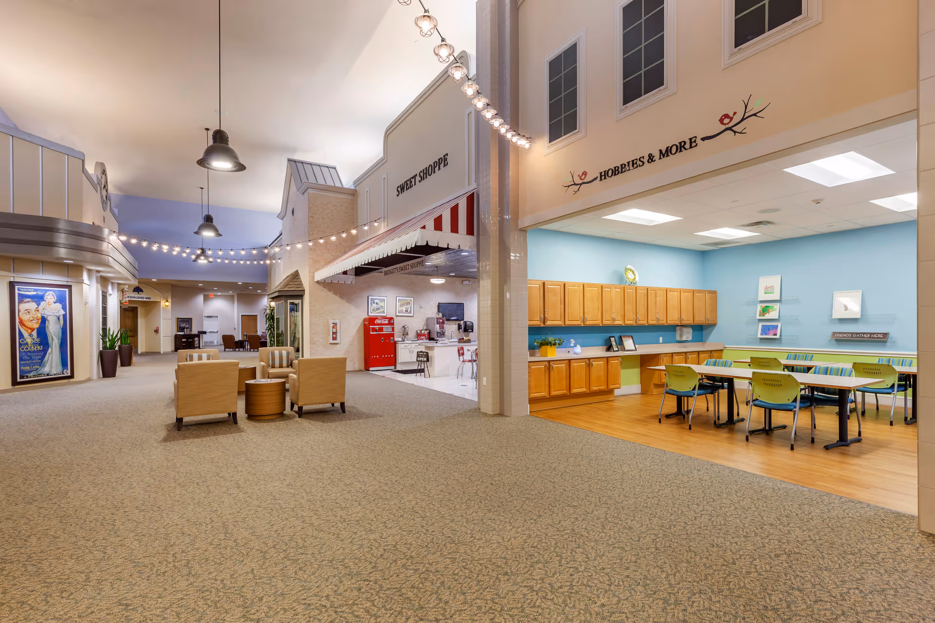 Spacious interior lobby of a senior living facility with seating, a Sweet Shoppe counter and a Hobbies & More activity room.