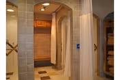 Interior view of a shower area with tiled walls and floors, featuring multiple shower stalls separated by curtains and a wooden bench in the background.