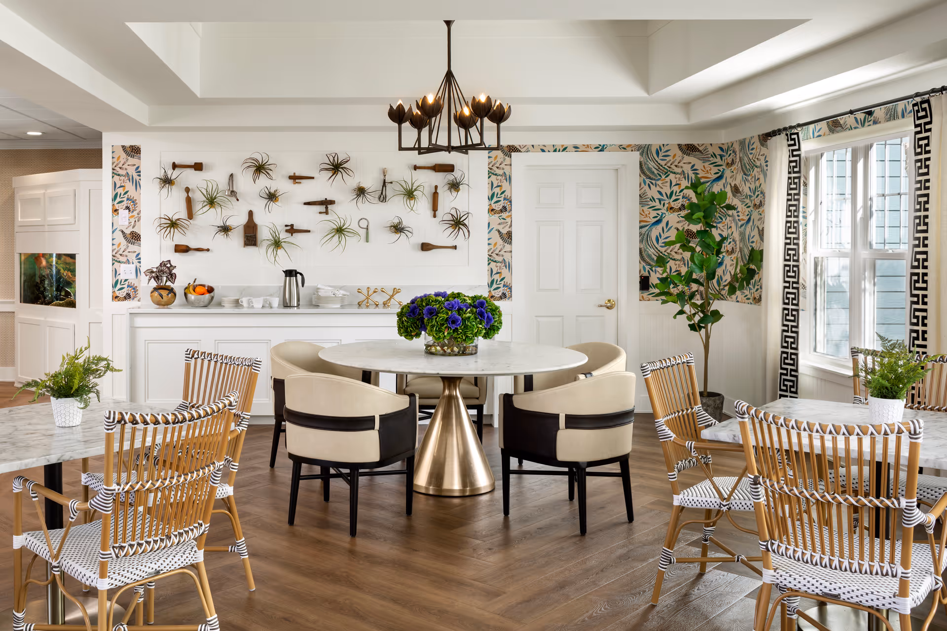 Bright, stylish communal dining room with a round marble table, mixed seating, wall-mounted plants and large windows.