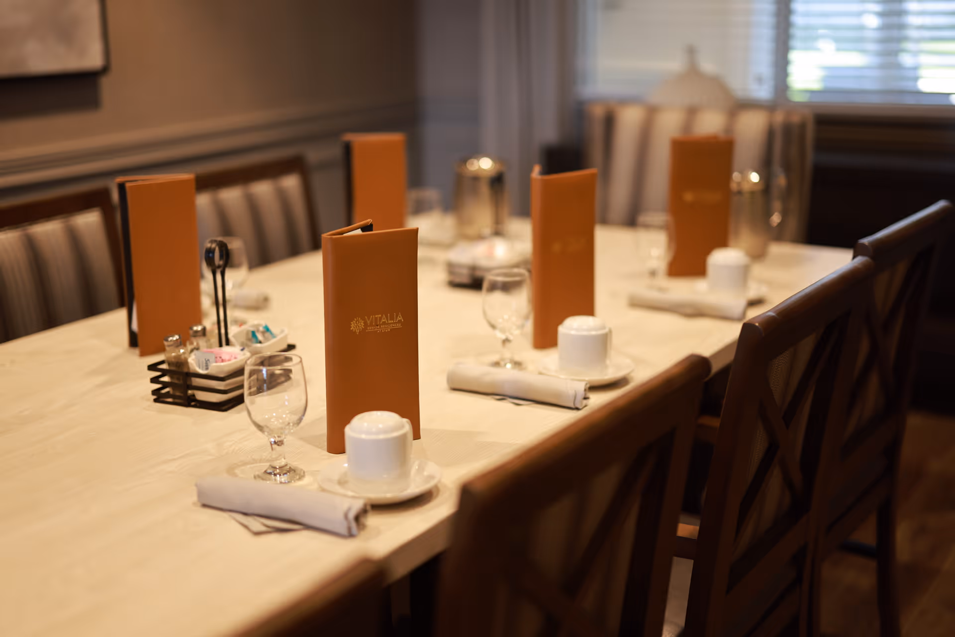 Dining room table set with brown Vitalia menus, glassware, cups, and folded napkins.