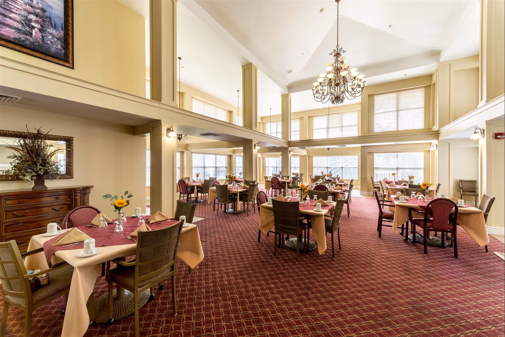 Spacious, well-lit dining room with multiple set tables, high ceilings, a chandelier, and large windows.