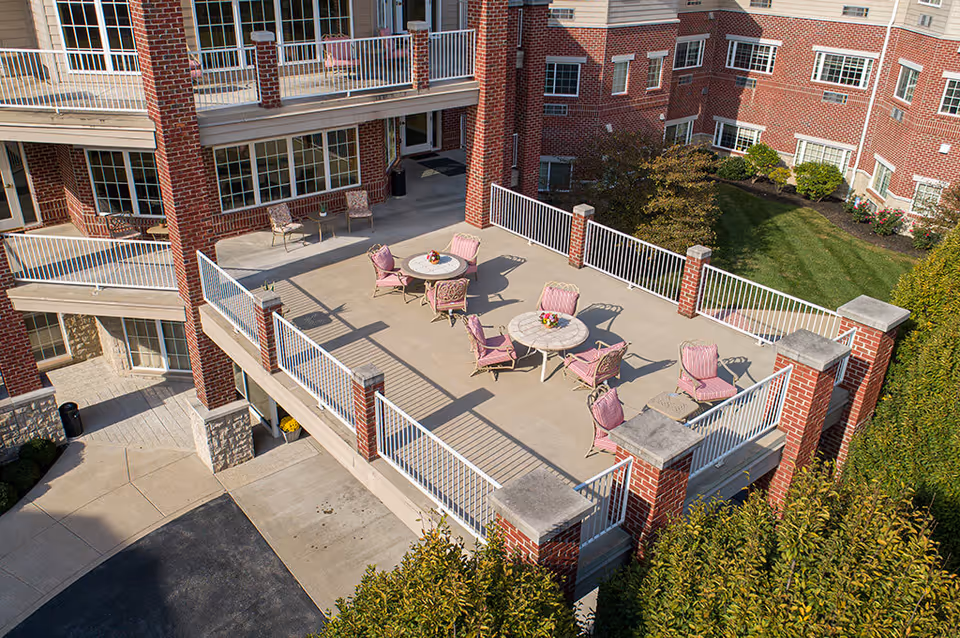 Elevated outdoor patio area with round tables and pink chairs on a concrete terrace surrounded by white railings and a brick building.