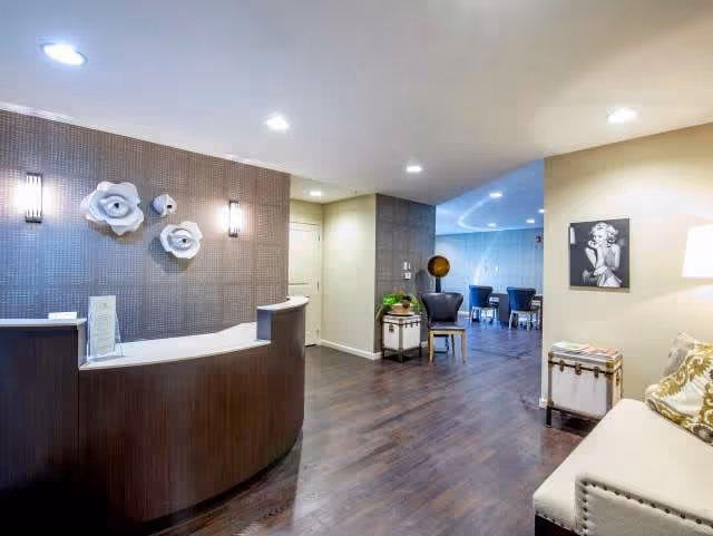 Reception lobby with a curved front desk, decorative wall flowers, and seating opening into a dining/lounge area.