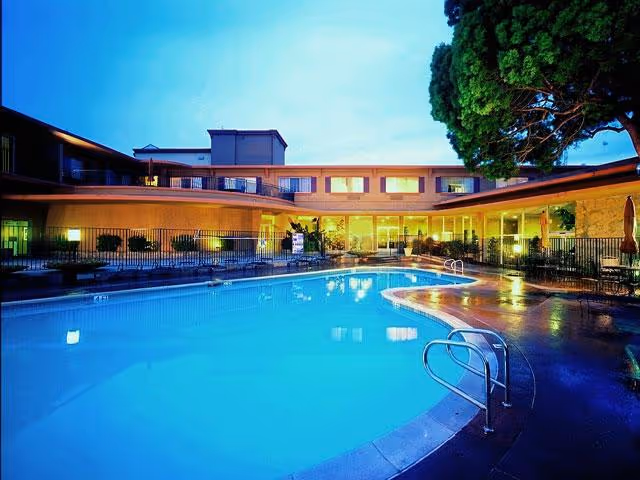 Curved outdoor swimming pool in the courtyard of a multi-story residential building lit at dusk.
