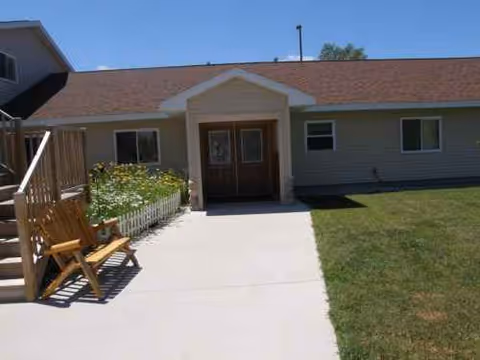 Front entrance of Culver Meadows Adult Foster Care with concrete walkway, bench, and flower bed.