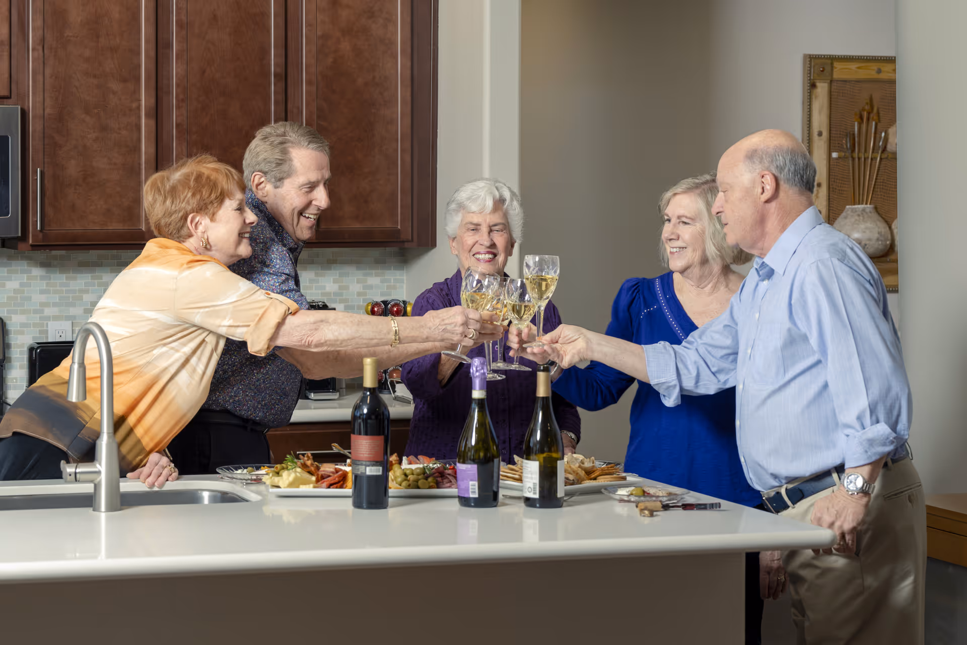 Five seniors toasting with glasses in a modern kitchen.