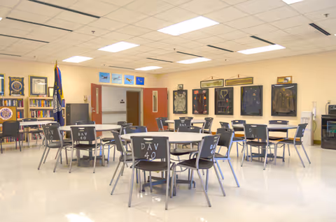 A bright indoor dining area with round tables and chairs, display boards on the walls, and a flag in the corner.