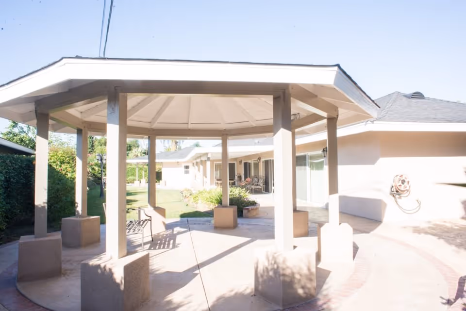 Sunlit octagonal gazebo with supporting columns in a courtyard next to a single-story assisted living building.