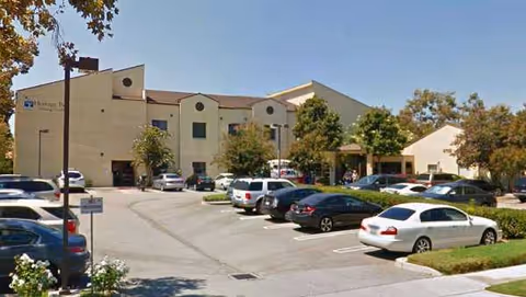 Exterior view of Heritage Park Nursing Center with a parking lot and trees.