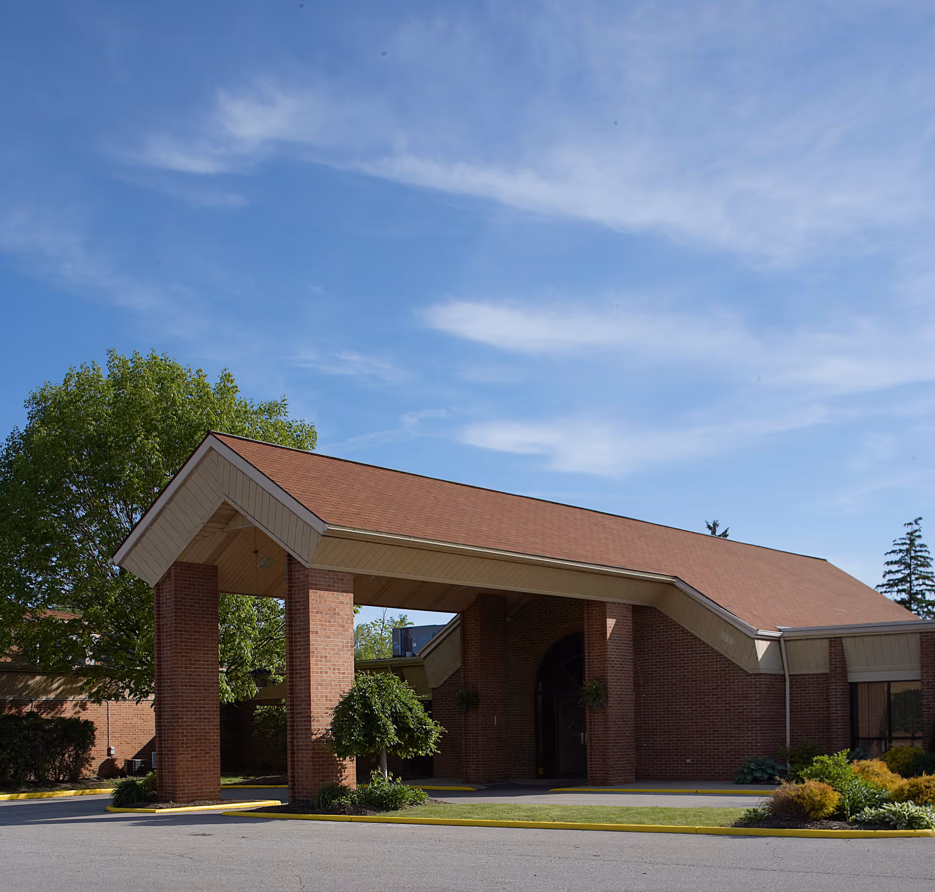 Covered entrance canopy of a brick building with columns, landscaping, and a clear blue sky.