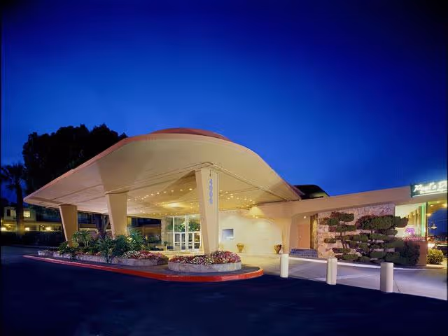 Exterior view of the entrance to Villa at San Mateo facility at dusk, featuring a large covered drop-off area with modern architectural design, landscaped plants, and illuminated building signage.