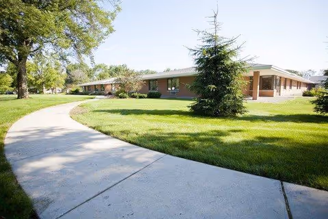 A single-story brick senior living facility with a curved walkway and green lawn.