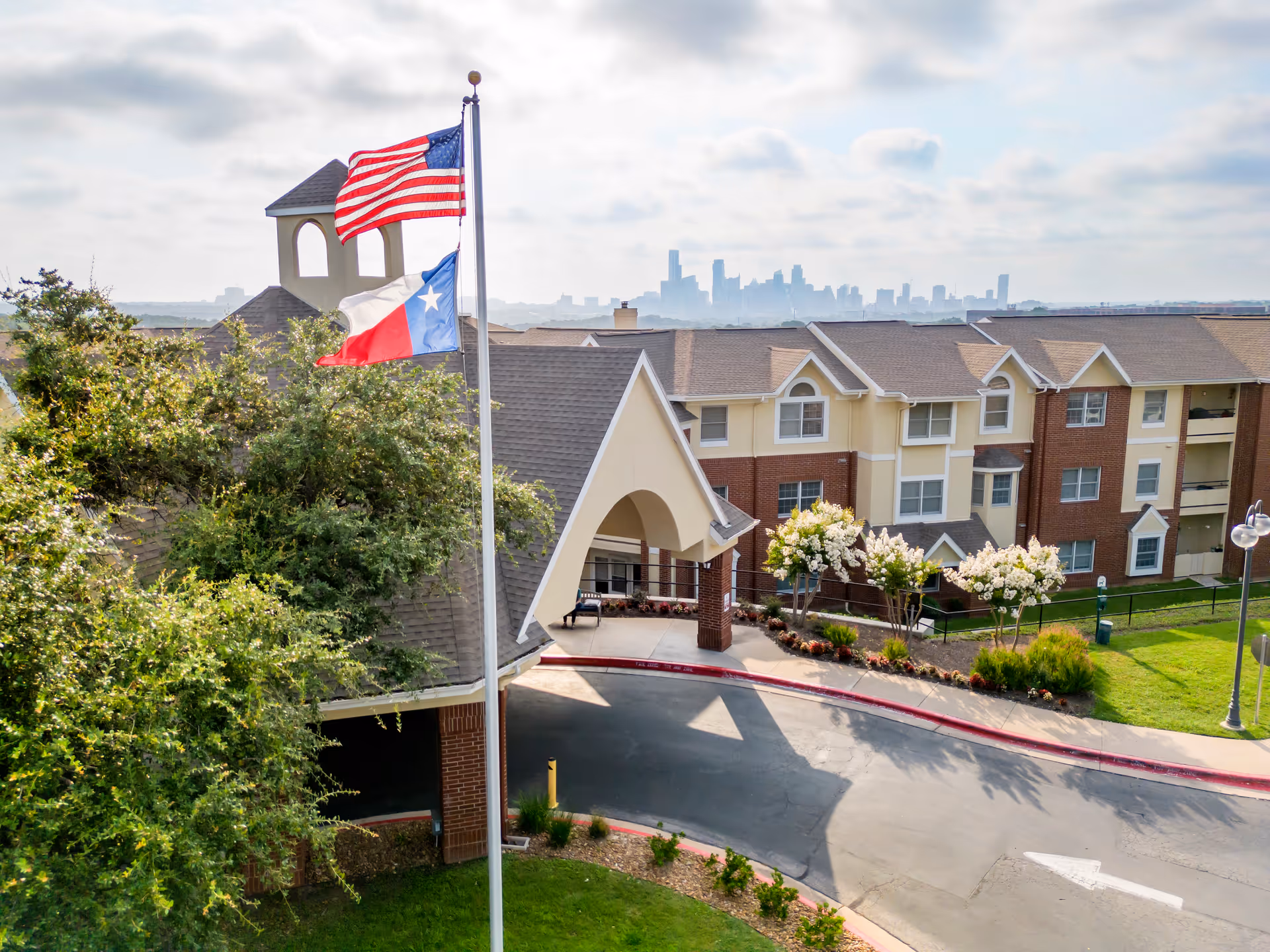 Flagpoles display US and Texas flags beside the entrance of a senior living complex.